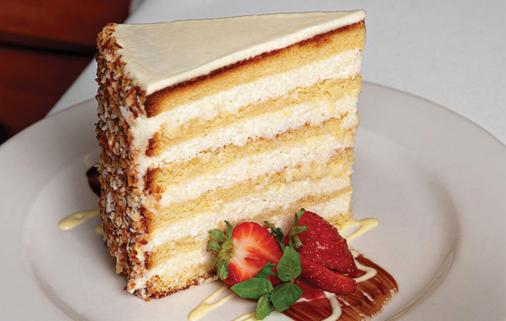 A slice of The Ultimate Coconut Cake on a plate, garnished with sliced strawberries