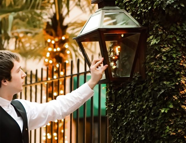 A restaurant server lighting carriage lights in the courtyard at Peninsula Grill